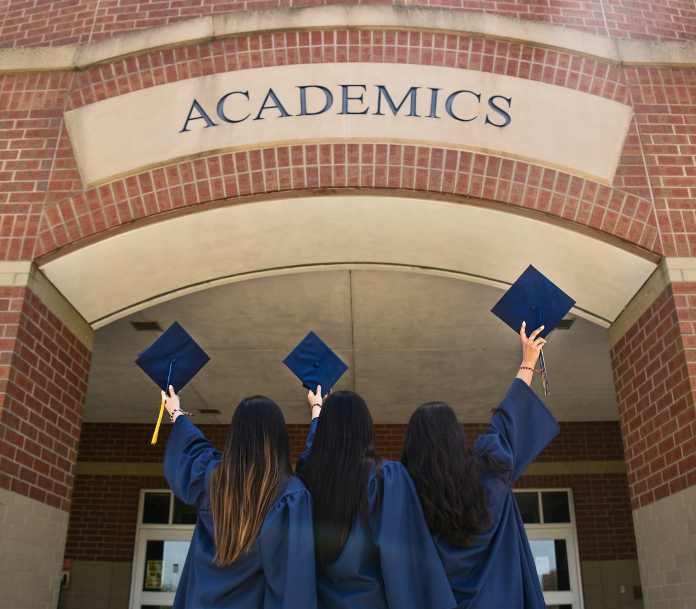 three girls in graduation gowns hold their caps in the air