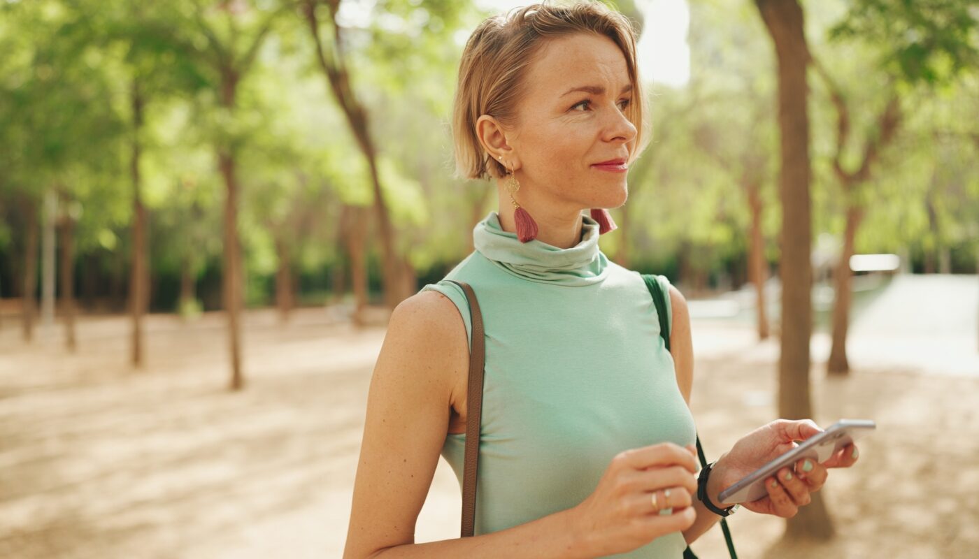 Beautiful smiling woman with short blond hair walks through the city square and using phone