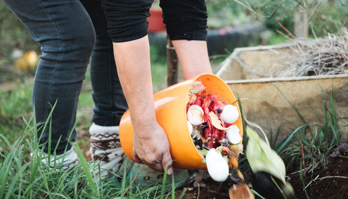 Person holding an orange bucket with compost and pouring into the soil in the rural garden