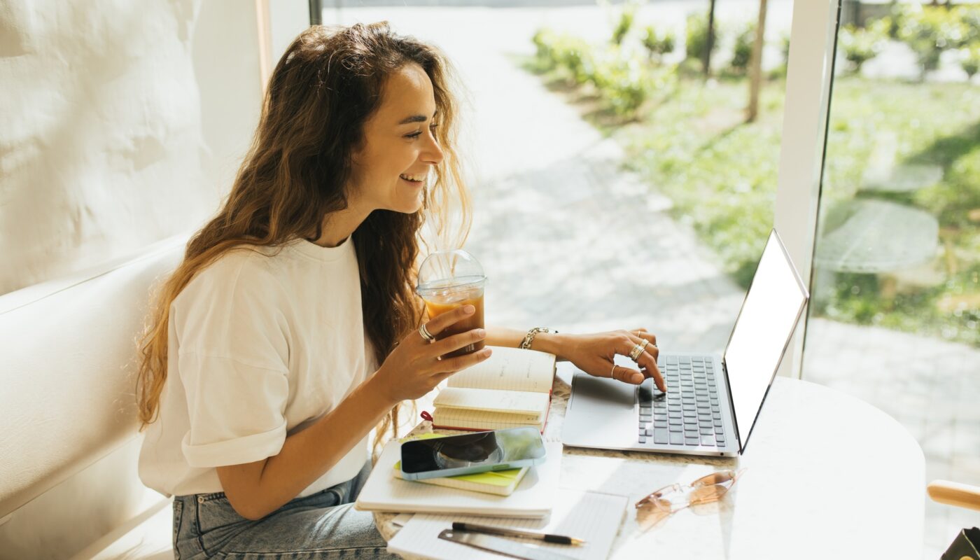 Young woman freelancer working in a coffeehouse, using her laptop and smartphone.
